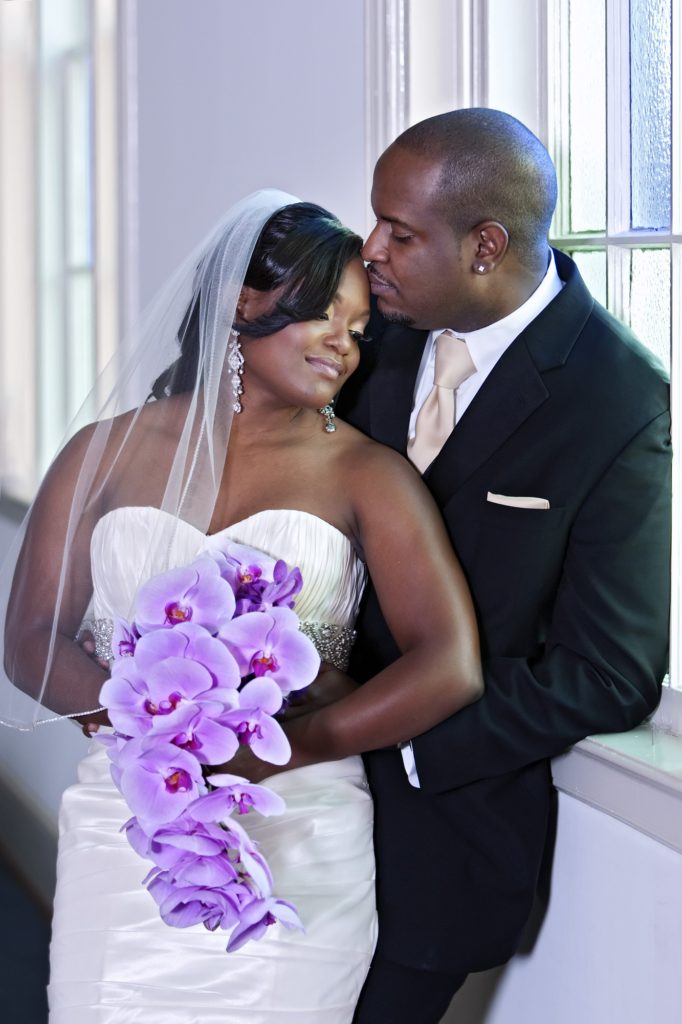 The Bride is holding a bouquet of purple orchids as she enjoys the company of her new husband.