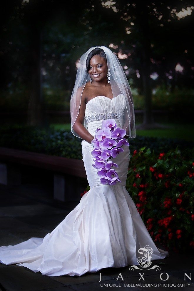 The bride is wearing a white mermaid dress with a embellished sash and the bouquet of purple orchids.