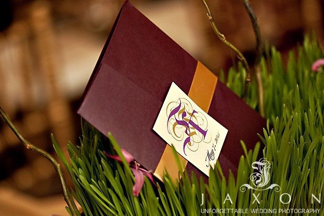 Plum colored Wedding Invitation wrapped in a gold band with monogrammed square attached in center