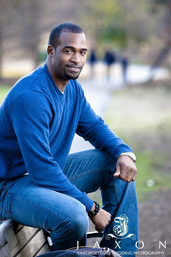 man wearing jeans and blue sweater sits on park bench