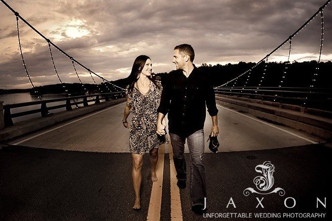 Couple walks with shoes in hand on the bridge against a late evening sky | Lake Lanier Engagement