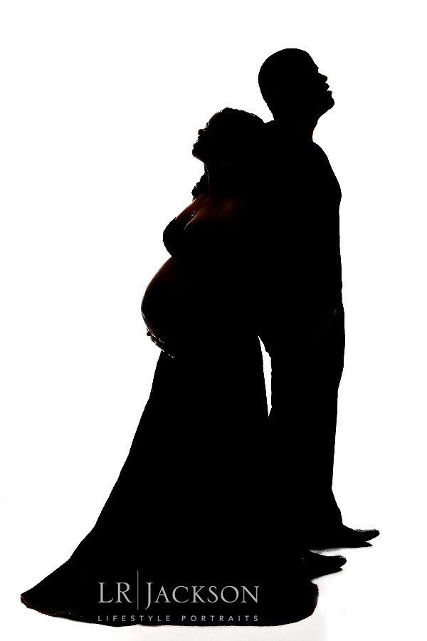 Silhouette of expectant couple back to back against a white background in studio 