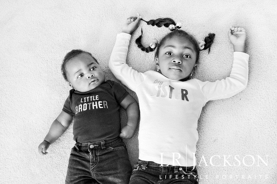 B&W Photograph of 1 year old brother with his 3yr old sister laying on the rug