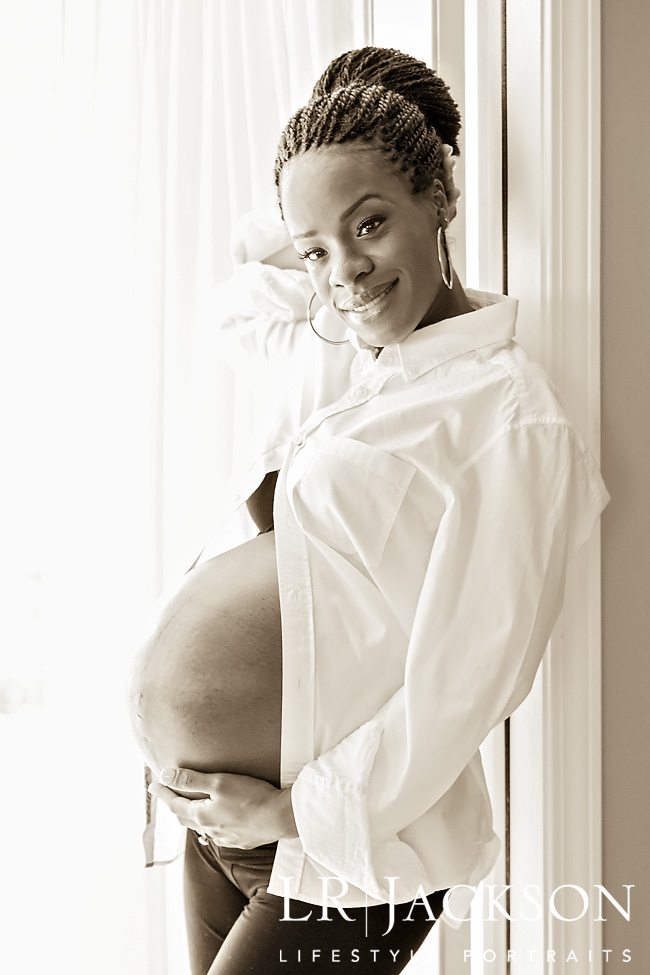 B&W portrait of pregnant woman leaning against door frame, she is wearing awhile open mans shirt with her belly exposed