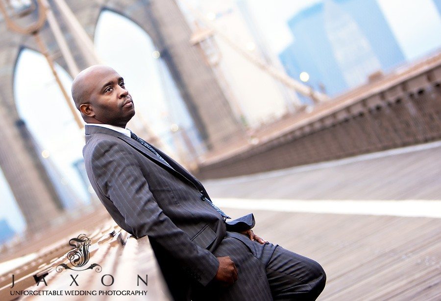 Groom leans on the railing on the Brooklyn Bridge, Manhattan outline id the background | Riviera Wedding Brooklyn, NY