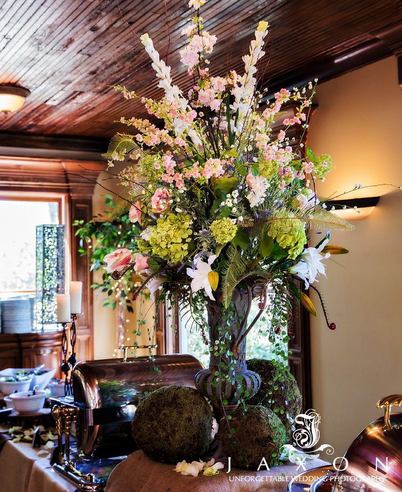 Buffet table floral arrangement with moss covered balls at base of metal urn vase topped with Hydrangeas, tulips, and lilies.