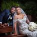 Bride sits and leans into groom as he rests on the back of park bench