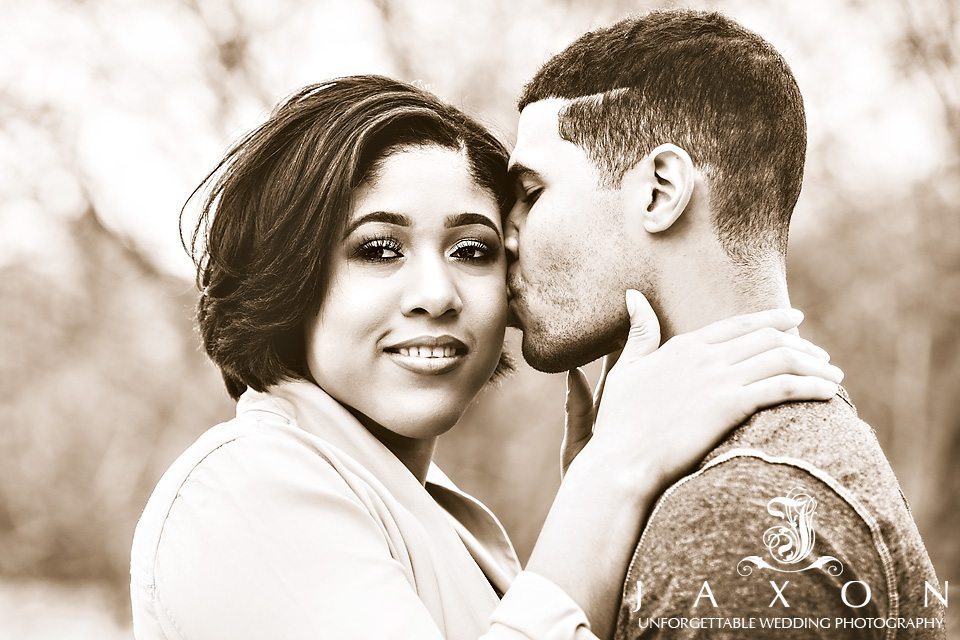 Sepia toned engagement photo of man kissing woman on the cheek as she looks pass camera