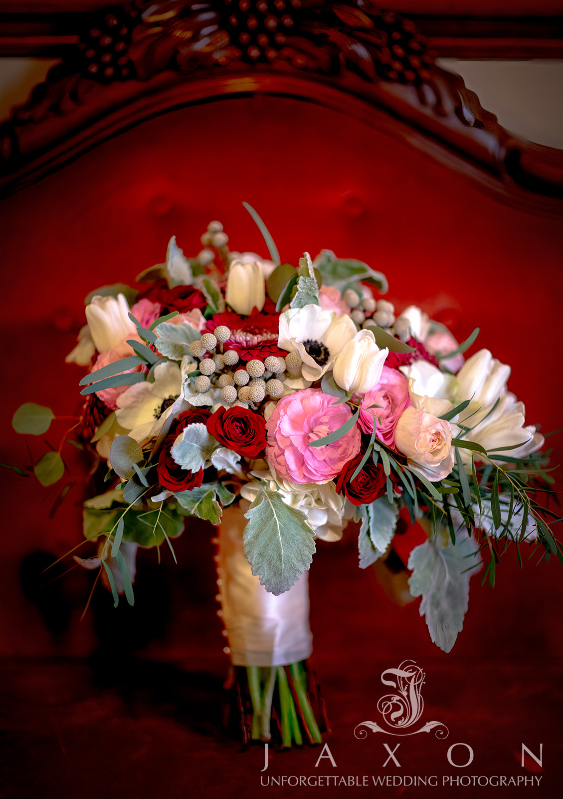 Bridal bouquet with white anemones, red roses, French tulips, hydrangea, and ranunculus on red loveseat at Carl House, Auburn, GA