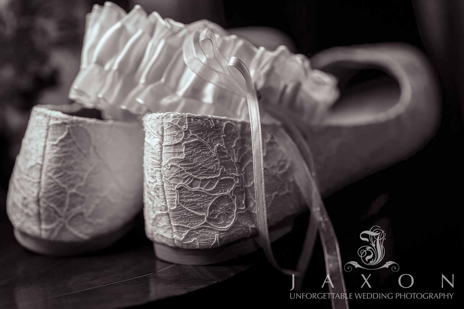 black and white photo of a bride's white floral lace pattern ballerina flats and garter, highlighting their intricate details and texture with side lighting before a Carl House Wedding in Auburn, GA.