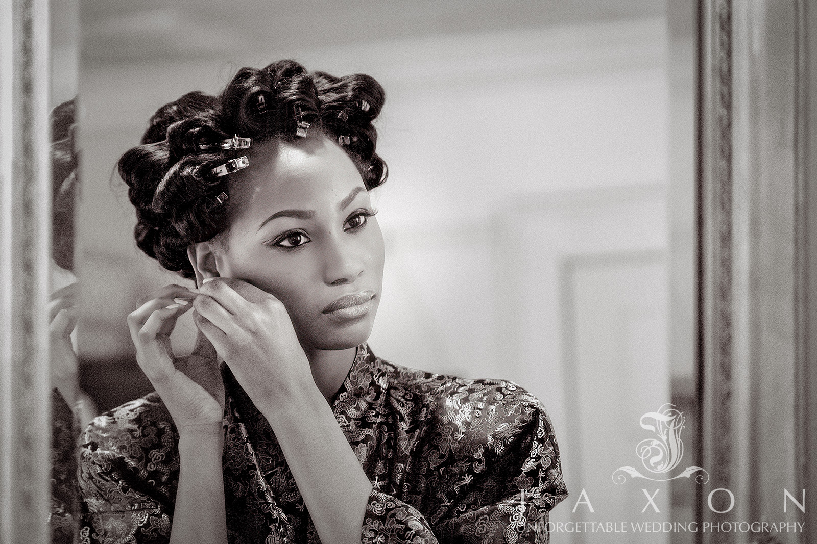 Bride putting on earrings in front of a mirror, wearing a silk robe with hair pinned up at Vines Mansion in Auburn, Georgia.