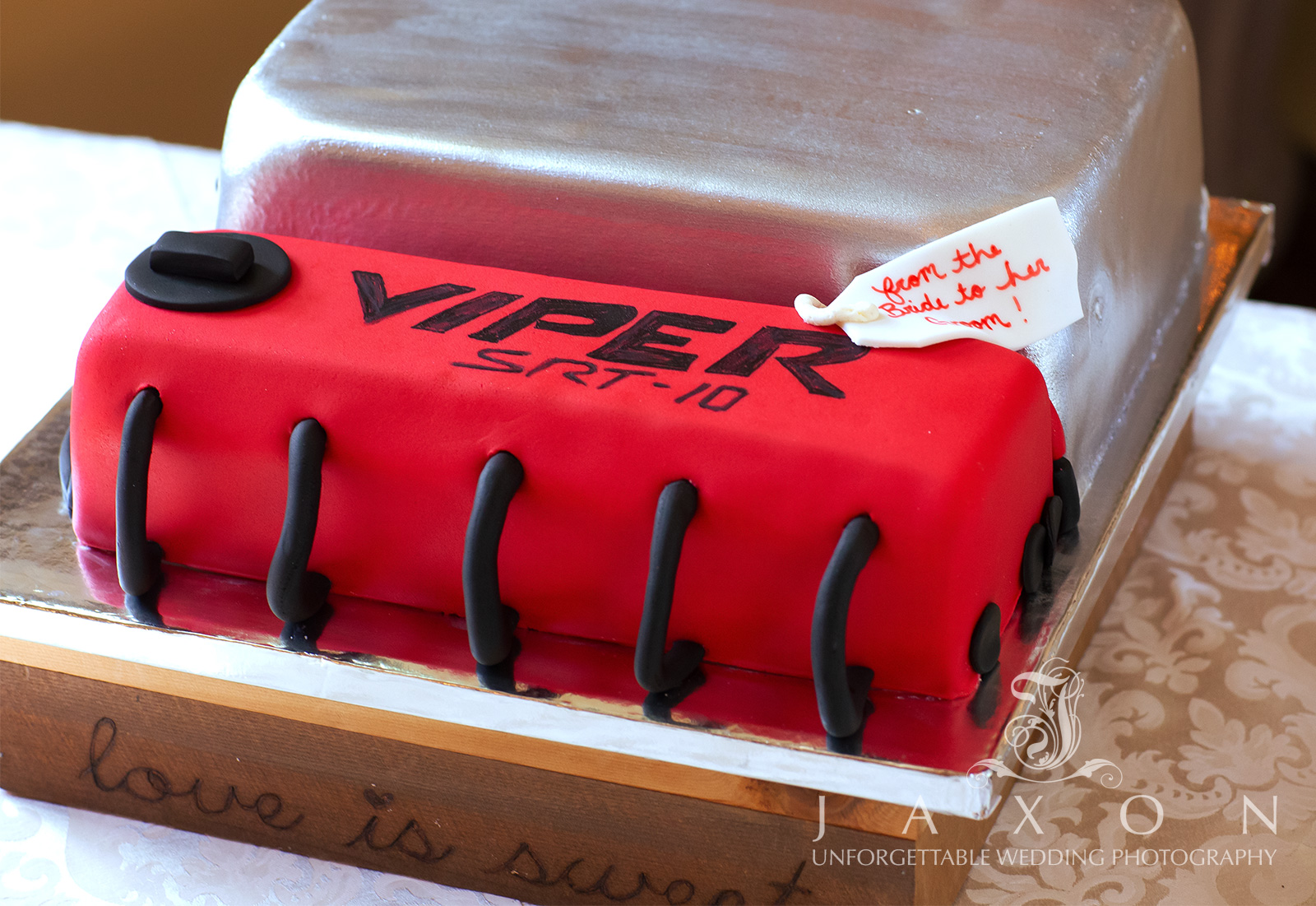 Unique groom's wedding cake designed to look like a Dodge Viper SRT 10 engine block, with silver, red, and black colors and a note reading 'from the bride to her groom.