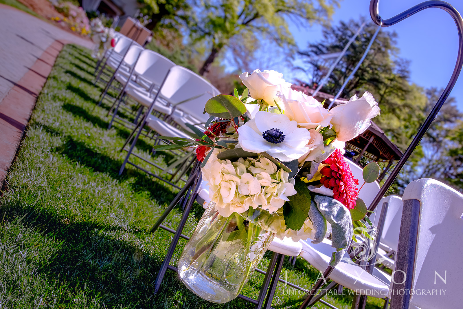 Garden wedding bouquet featuring white anemones, red roses, French tulips, hydrangea, and ranunculus in a mason jar hanging outdoors at Carl House, Auburn GA.