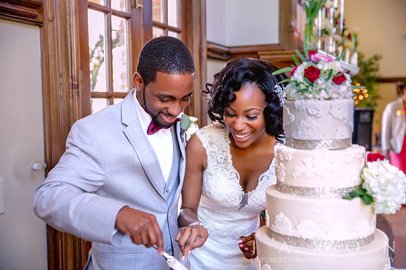 Elegant four-tiered wedding cake with white lace embroidery and vibrant floral decorations at Carl House Wedding Venue